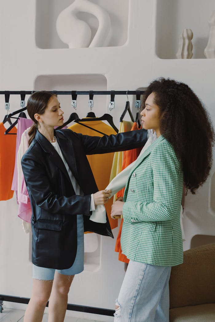 Two women collaborating on fashion styling, exploring wardrobe choices with vibrant clothing options.